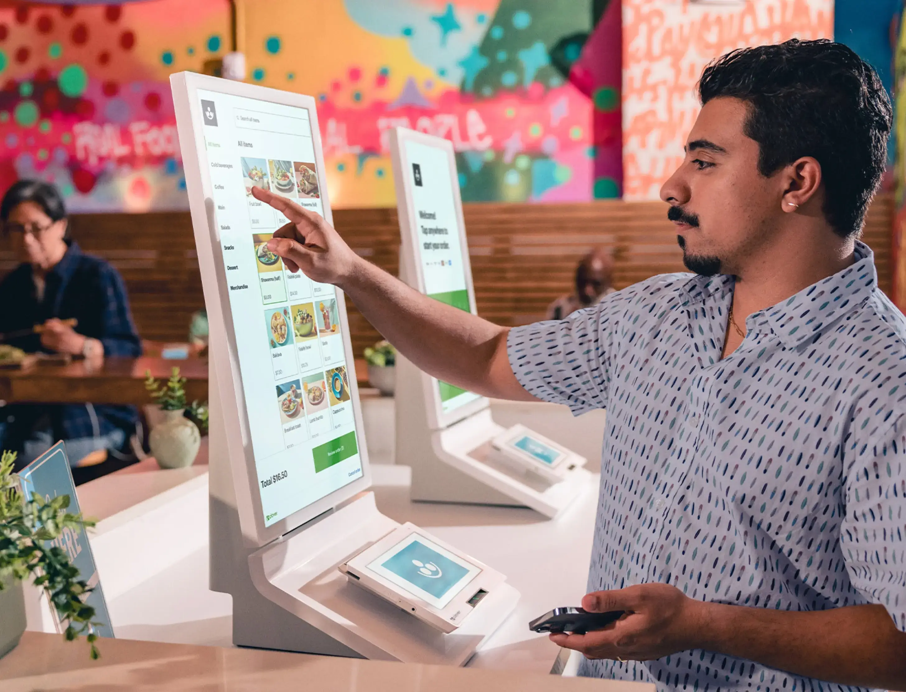 Customer using a Clover self-order kiosk in a colorful counter-service restaurant