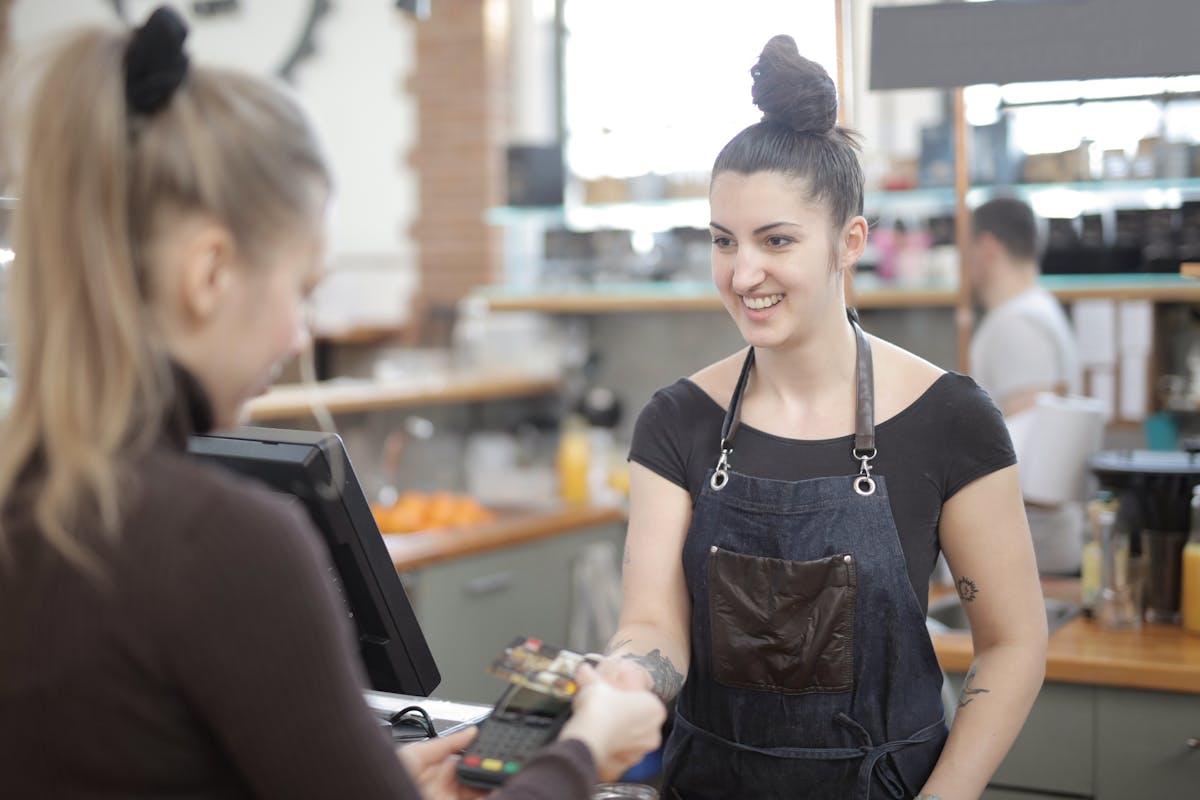 Smiling cafe owner handing back a card payment terminal to a happy customer — real Infinity Pay merchant moment
